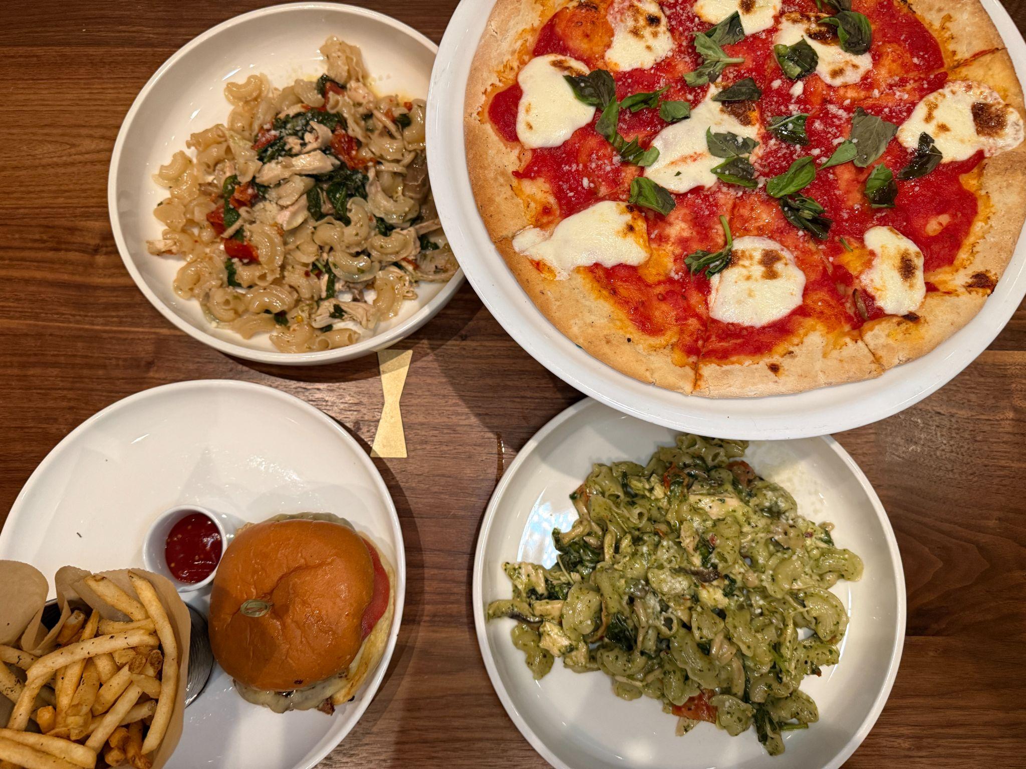 Spread of Sixty Vines dishes including a margherita pizza, pasta, and a burger with fries