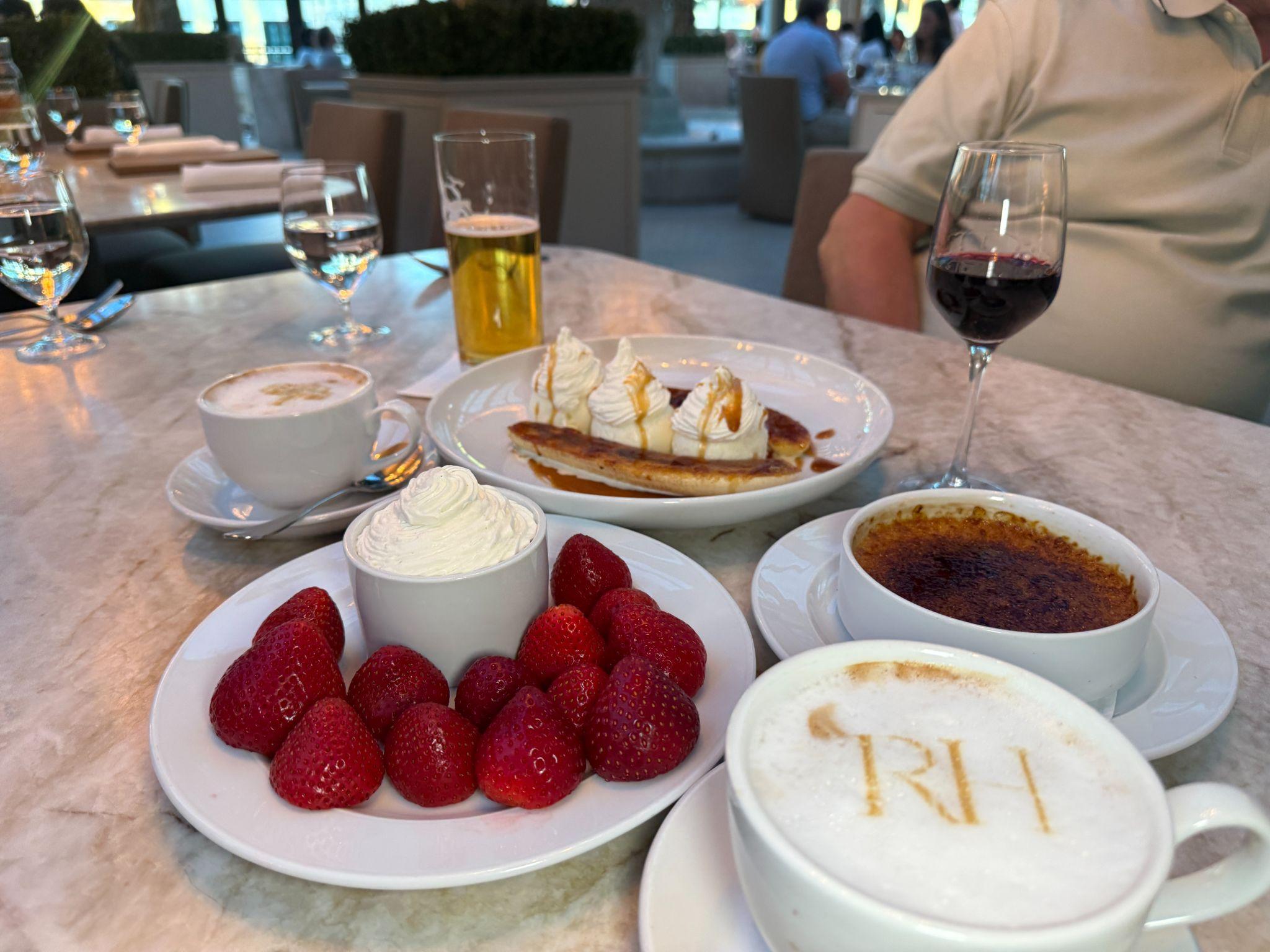 Dessert at RH Rooftop Restaurant Raleigh — strawberries with cream, crème brûlée, and RH cappuccinos on a marble table