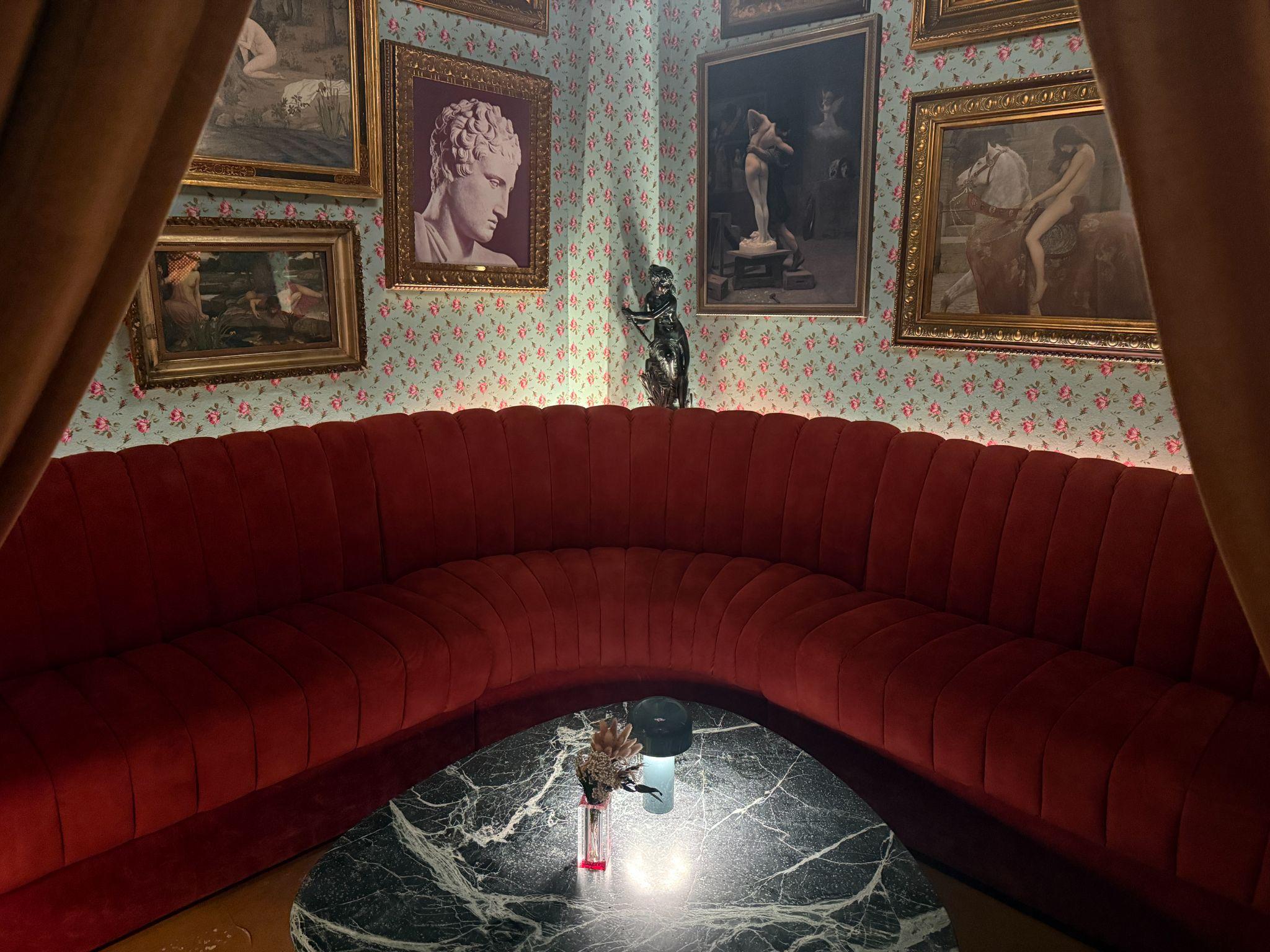 Romantic red-velvet curved booth at Capulet Cocktail Club with framed classical art and a marble table