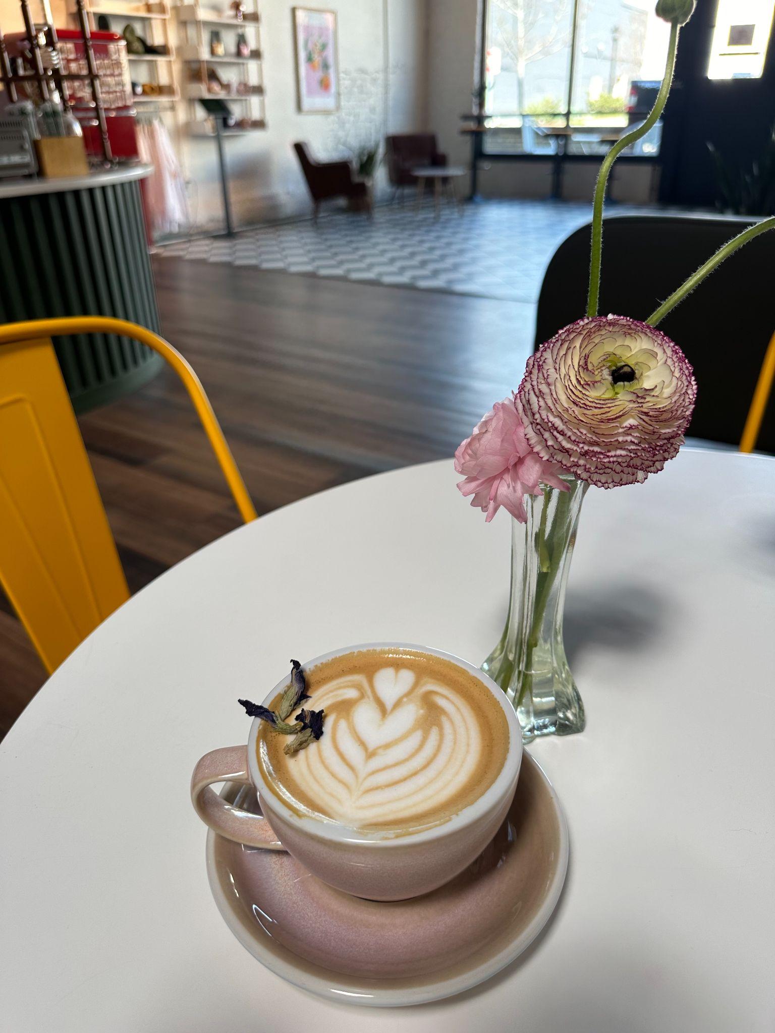 Latte with heart-shaped foam art beside a small vase of ranunculus at Parallax Coffee Lab in downtown Wendell
