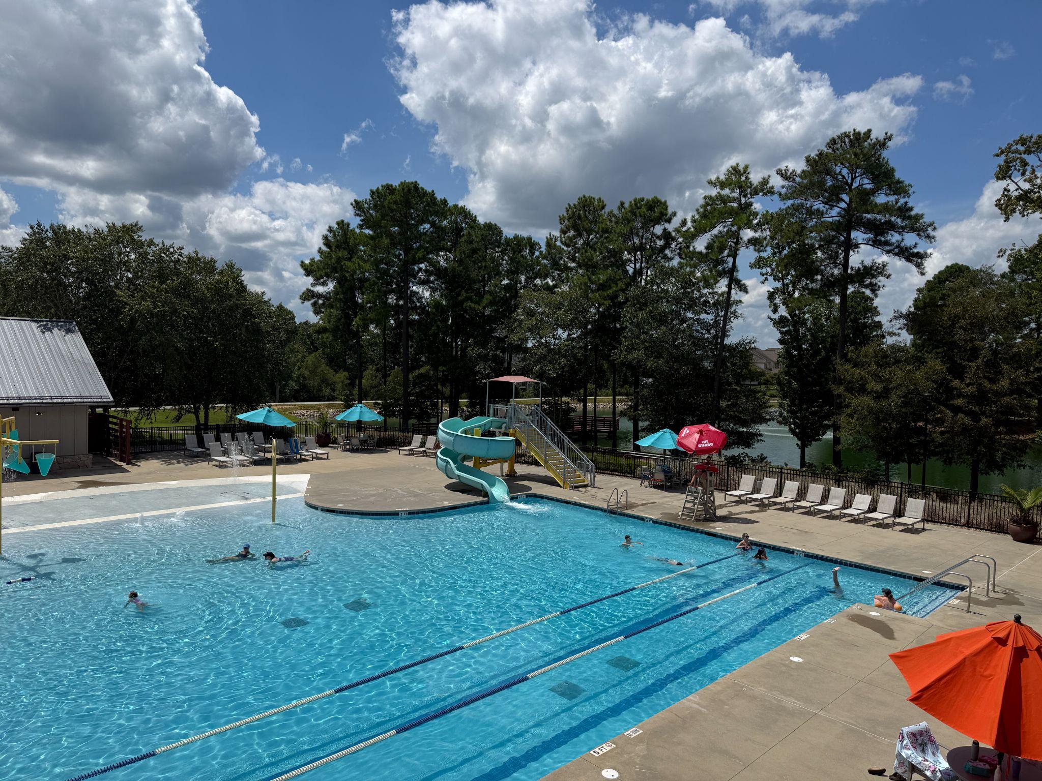 Resort-style community pool with a water slide and lake views at Wendell Falls on a sunny day