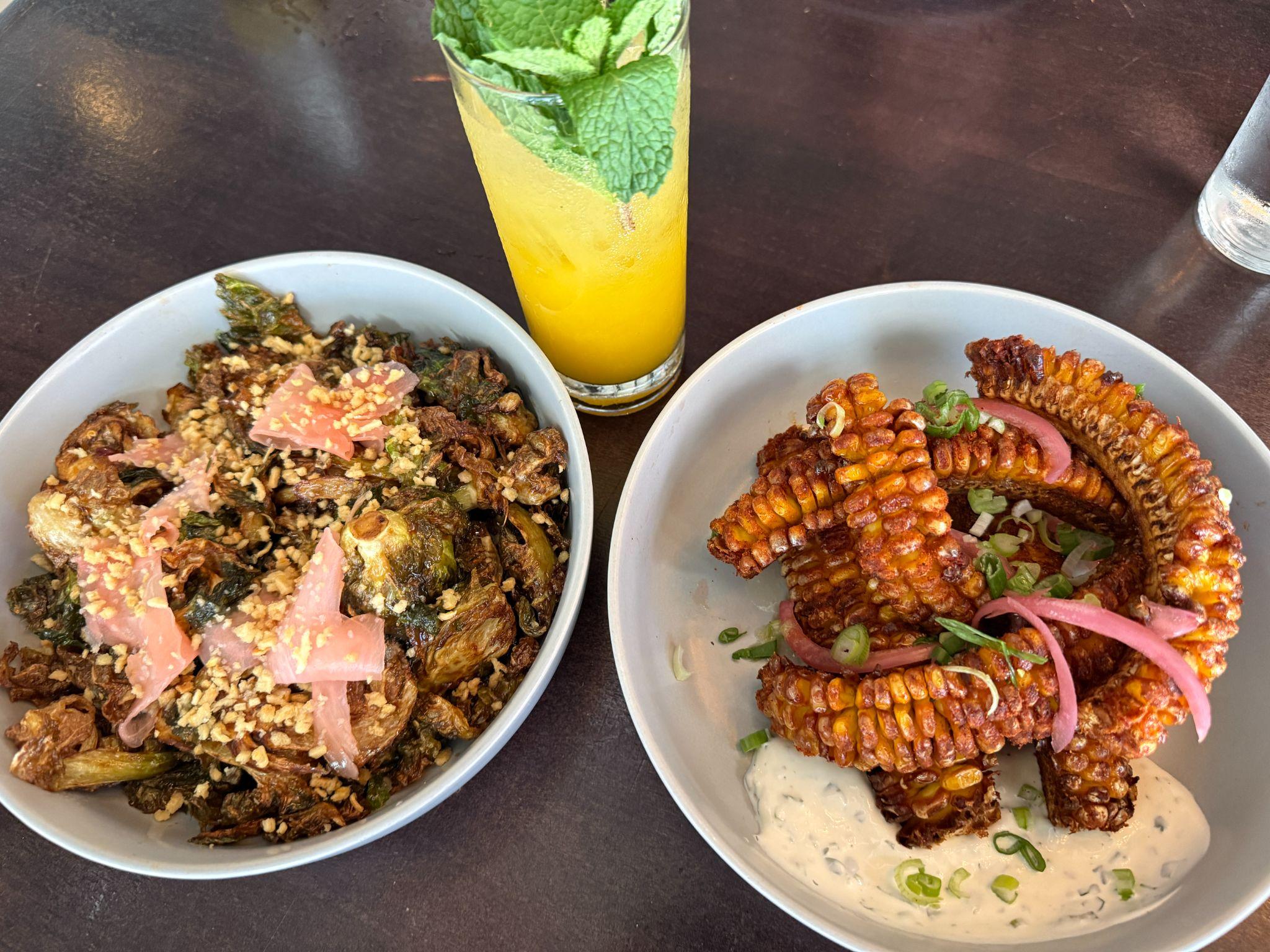 Crispy Brussels sprouts, loaded crinkle-cut fries, and a citrus cocktail on a table at Crescendo in Clayton