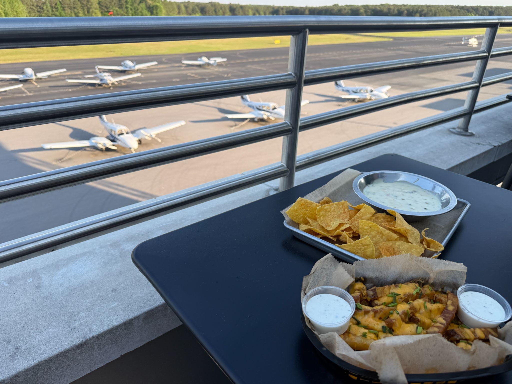 Chips and queso on a patio table at Low and Slow Smokehouse with small planes parked on the Johnston Regional Airport runway behind
