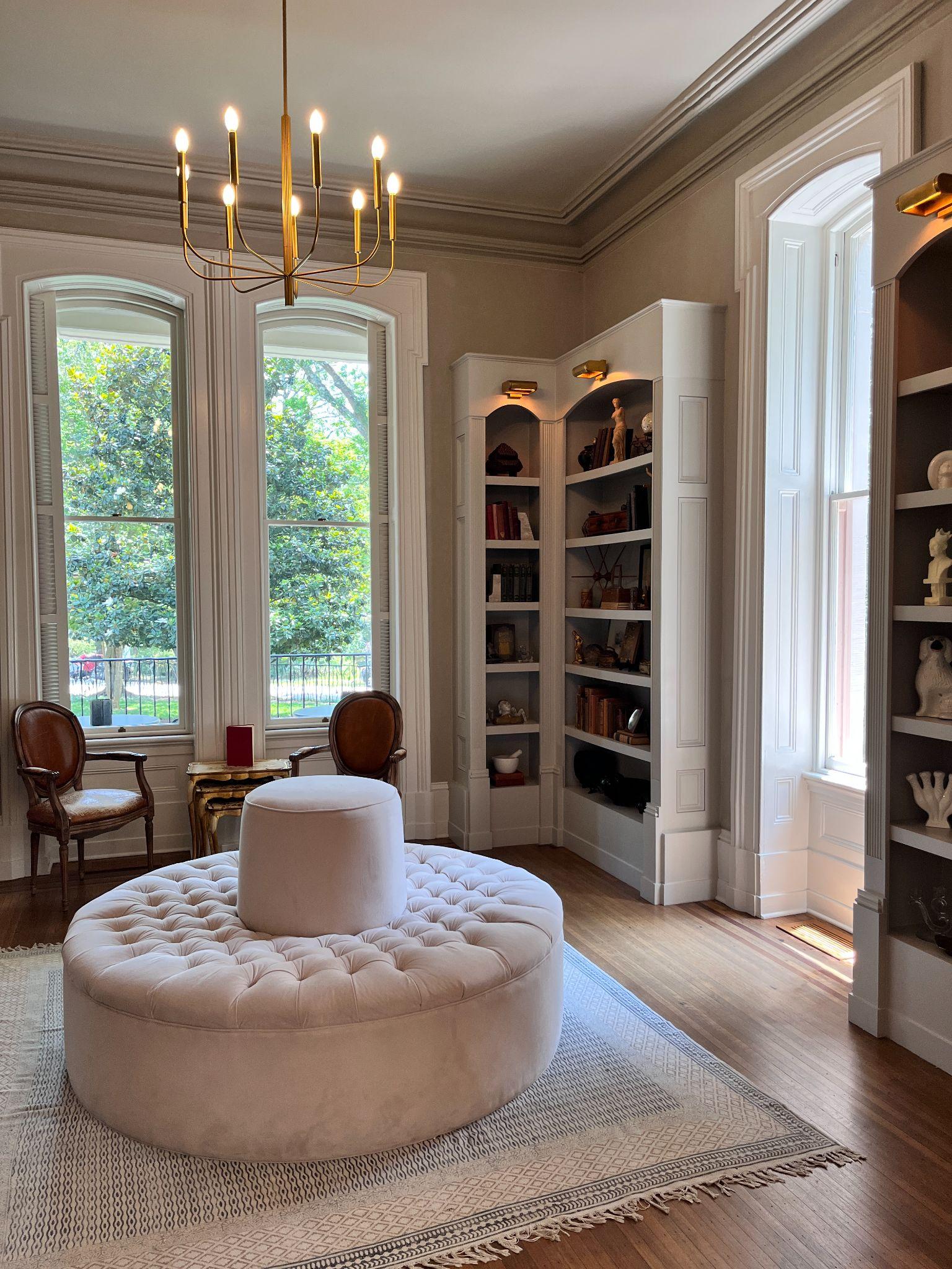 Elegant parlor at Heights House with tall arched windows, built-in bookshelves, a brass chandelier, and a tufted round settee