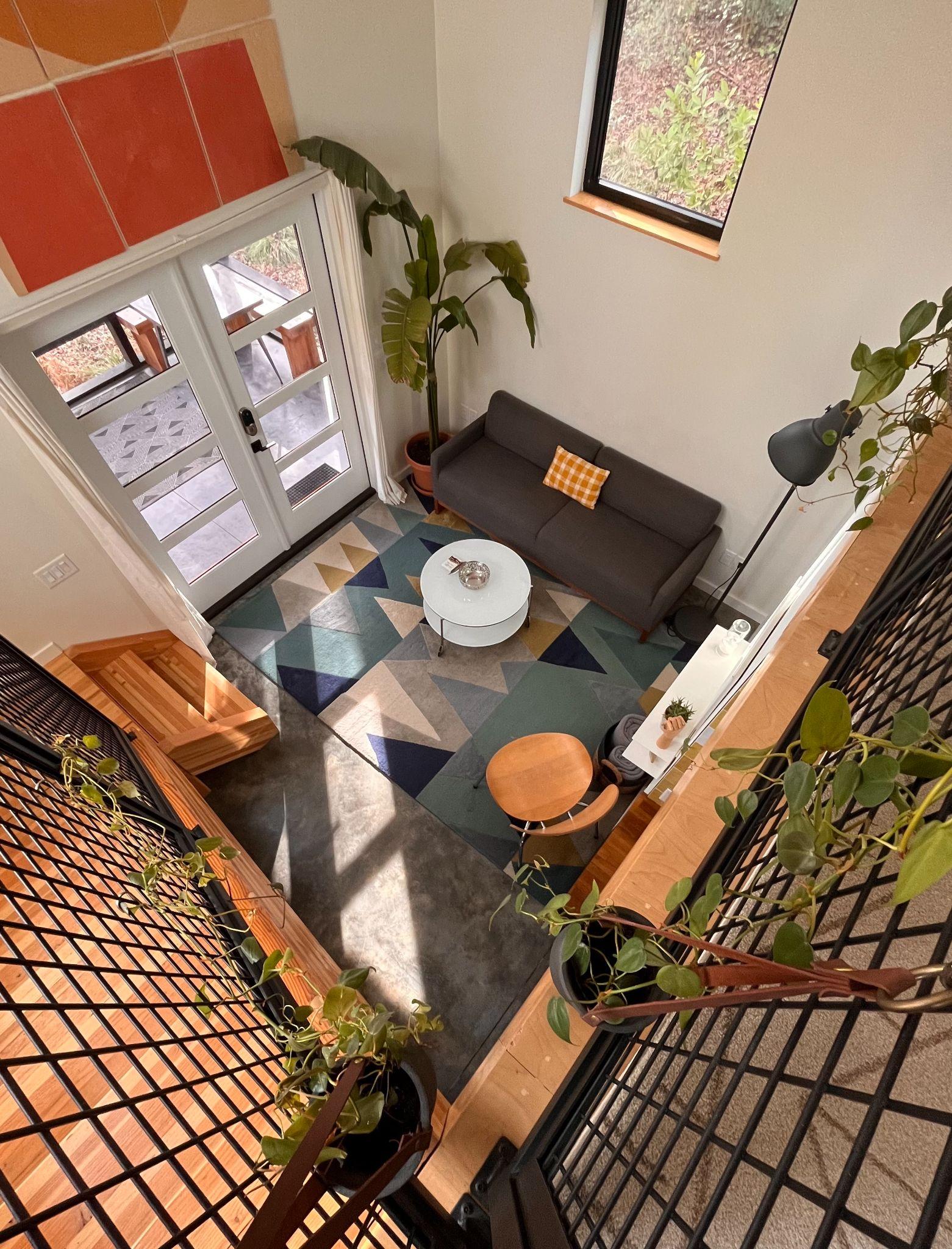 Interior of a modern tiny house near Durham seen from the loft, with a gray sofa, geometric rug, and abundant houseplants