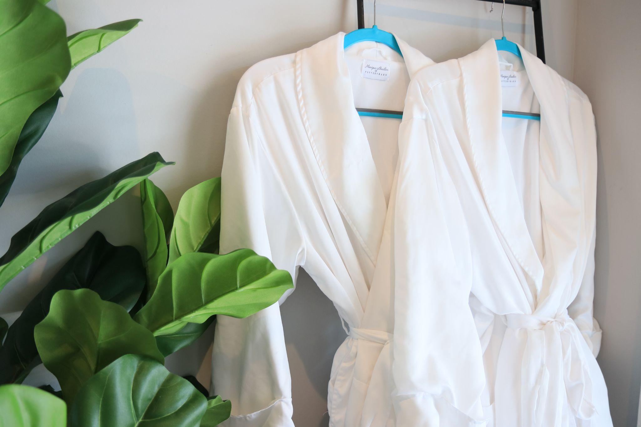 Two white robes on hangers beside a leafy houseplant inside the Farmhouse at Scout