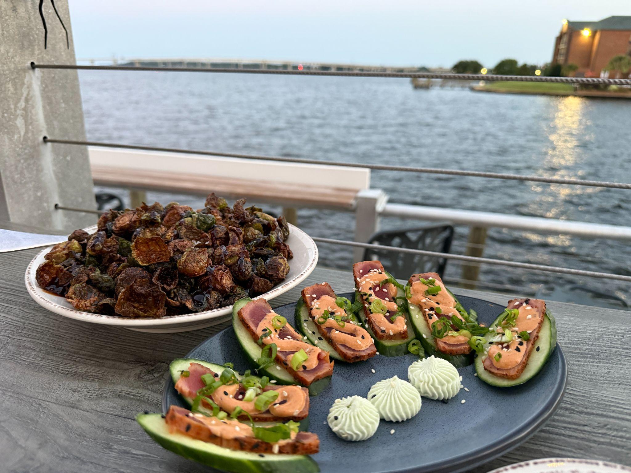 Seared tuna cucumber bites and crispy Brussels sprouts on a waterfront restaurant table overlooking the river in New Bern