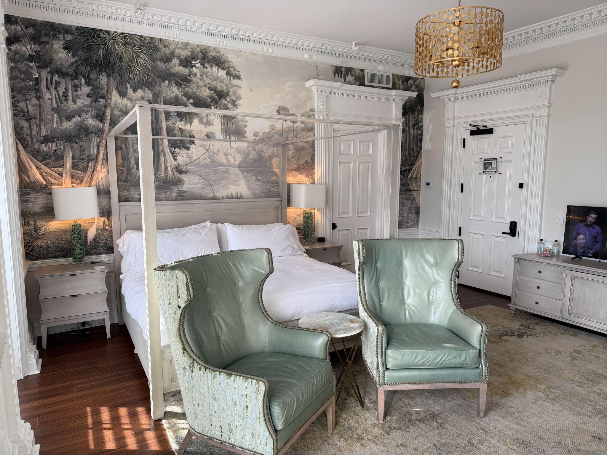 Boutique guest room at The Harvey in downtown New Bern with a canopy bed, riverside mural, and sage-green leather chairs