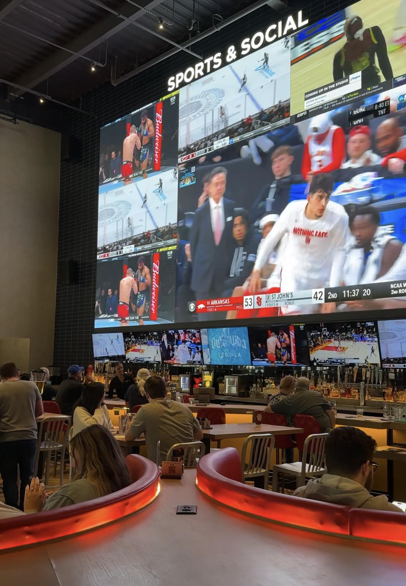 Wall of large screens inside Sports and Social Cary at Fenton showing multiple live sports broadcasts