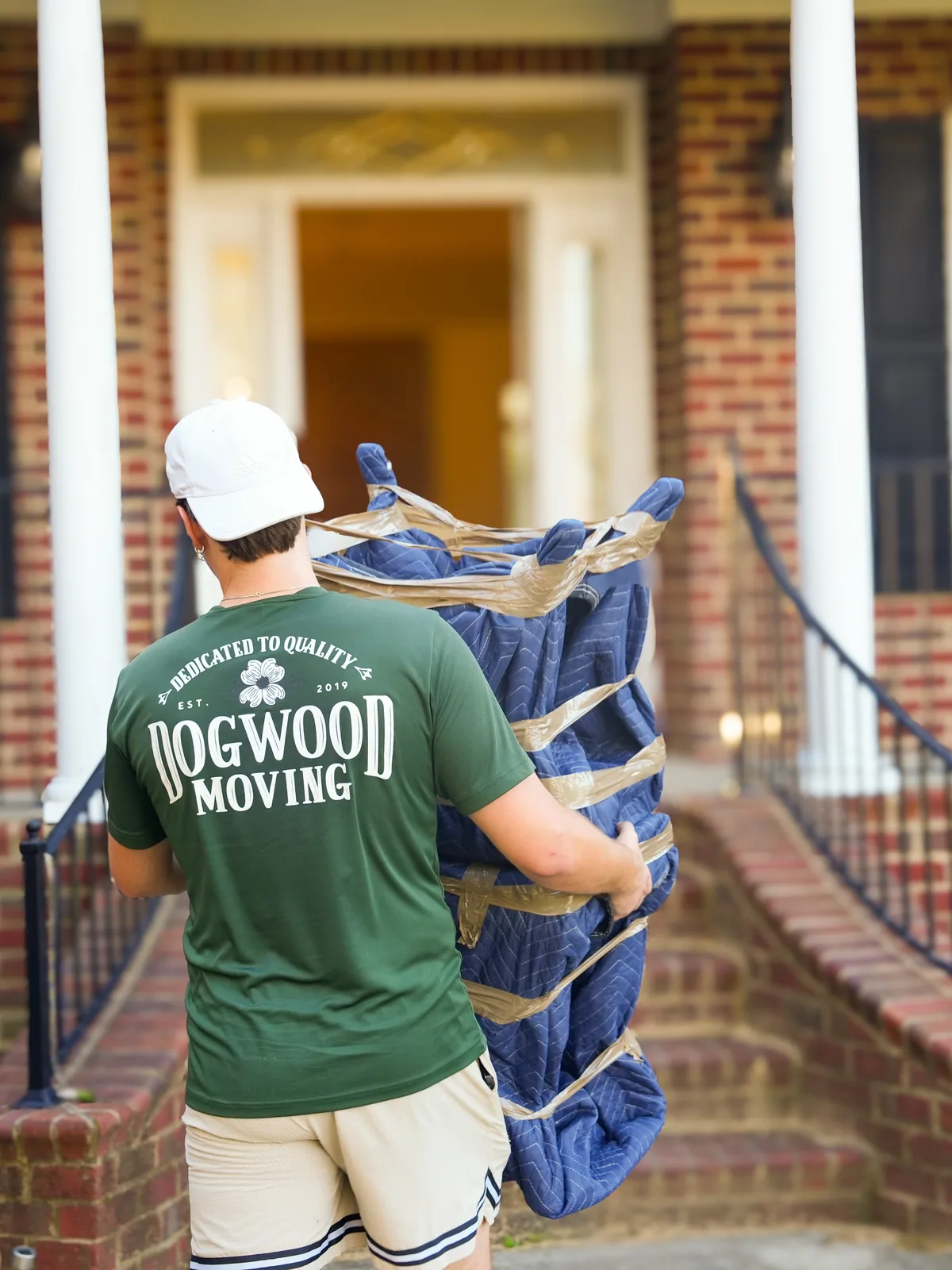 Dogwood mover carrying wrapped mattress up the steps of a home